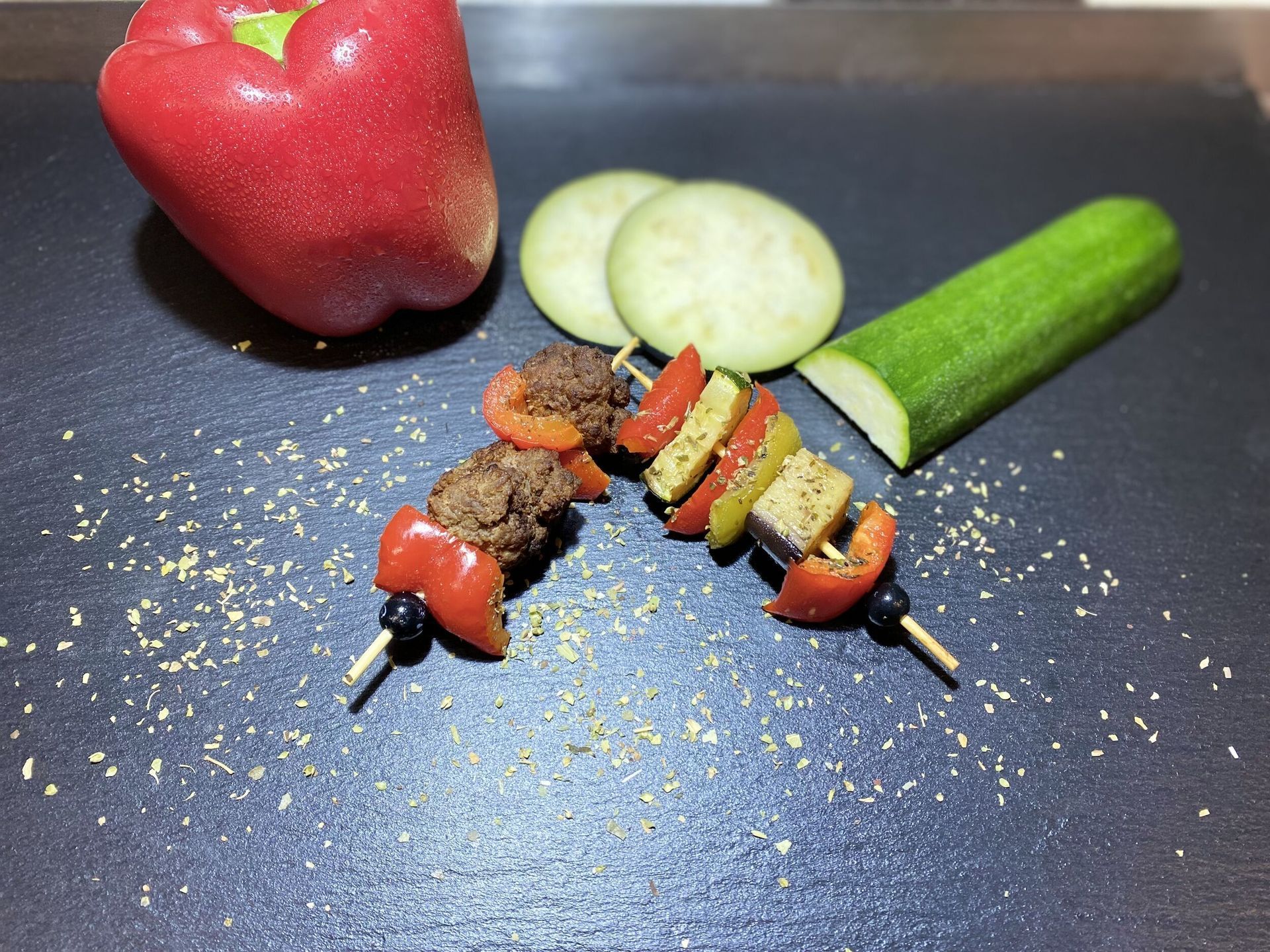 Zwei Spieße mit Fleisch und Gemüse auf einer schwarzen Oberfläche