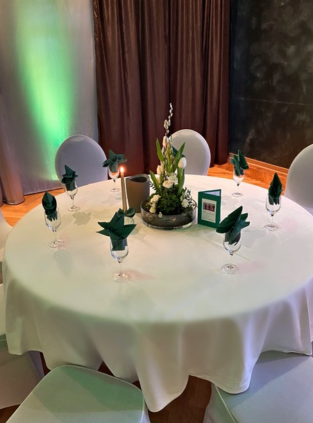 Ein runder Tisch mit einer weißen Tischdecke und einer Vase mit Blumen darauf.
