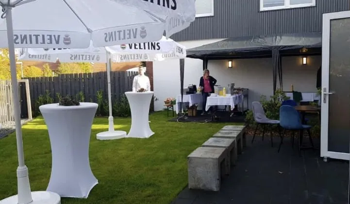 Ein Mann steht in einem Hinterhof mit Tischen und Sonnenschirmen.