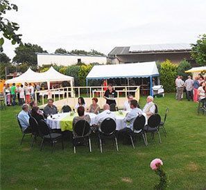 Eine Gruppe von Menschen sitzt auf einer Wiese um Tische herum.