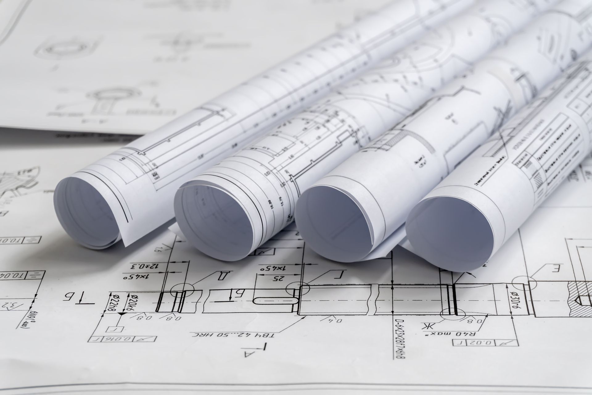 Drei zusammengerollte Baupläne liegen auf einer flachen, entfalteten technischen Architekturzeichnung.