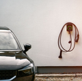 Ein schwarzes Elektrofahrzeug parkt neben einer weißen Wand, an der eine Wallbox-Ladestation mit einem aufgerollten Kabel montiert ist.