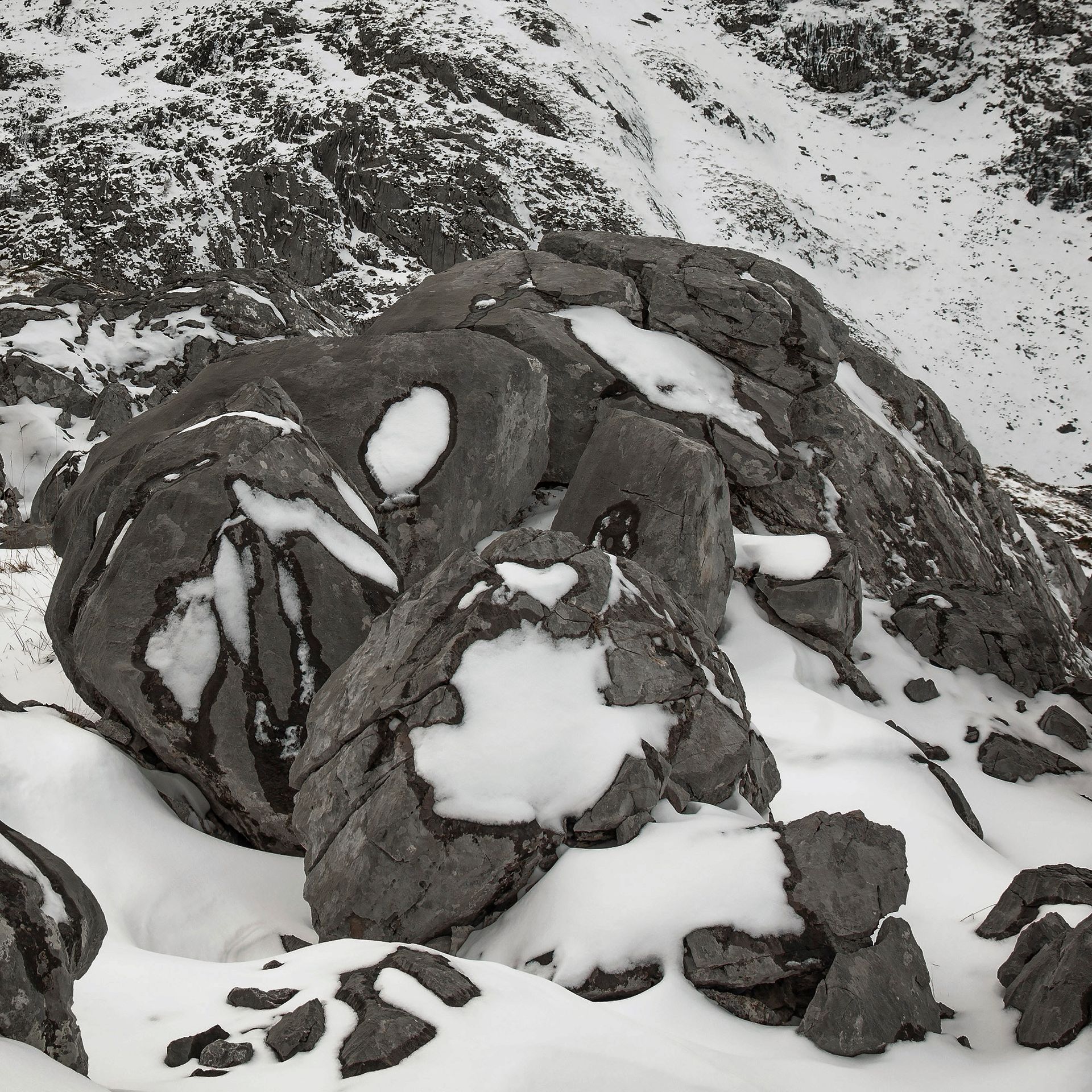 Rocas cubiertas de nieve en un paisaje montañoso, con parches de nieve y un fondo nevado.