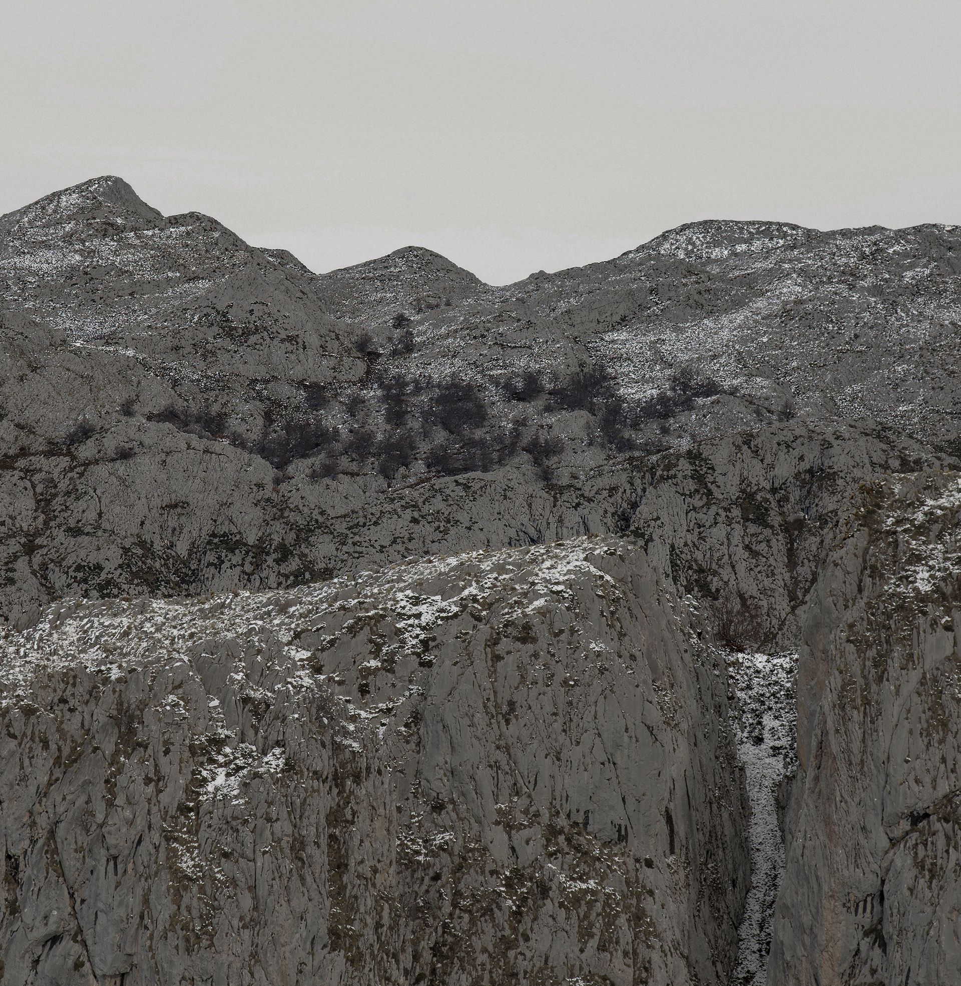 Cordillera rocosa con parches de nieve bajo un cielo nublado.