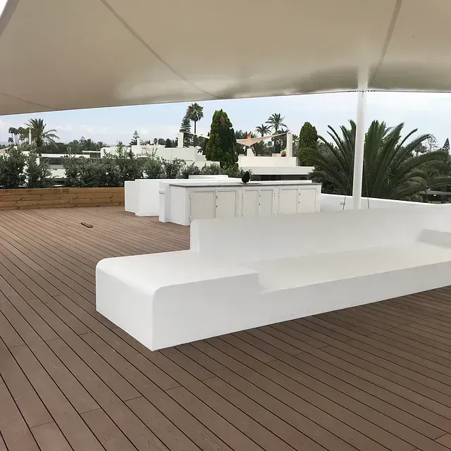 Un sofá blanco se encuentra en una terraza de madera bajo una sombrilla.