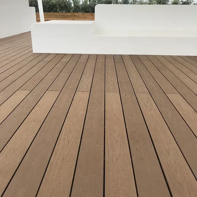 Una terraza de madera con un banco blanco al fondo.