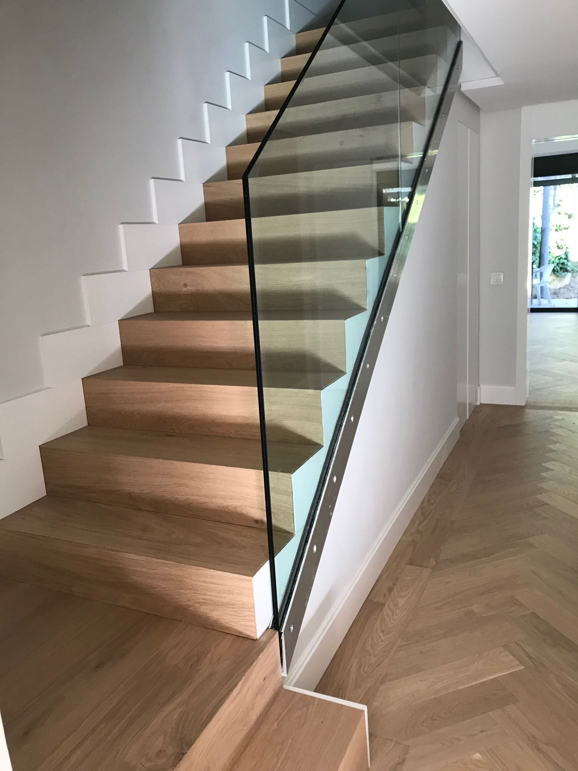 Una escalera de madera con barandilla de vidrio en un pasillo.