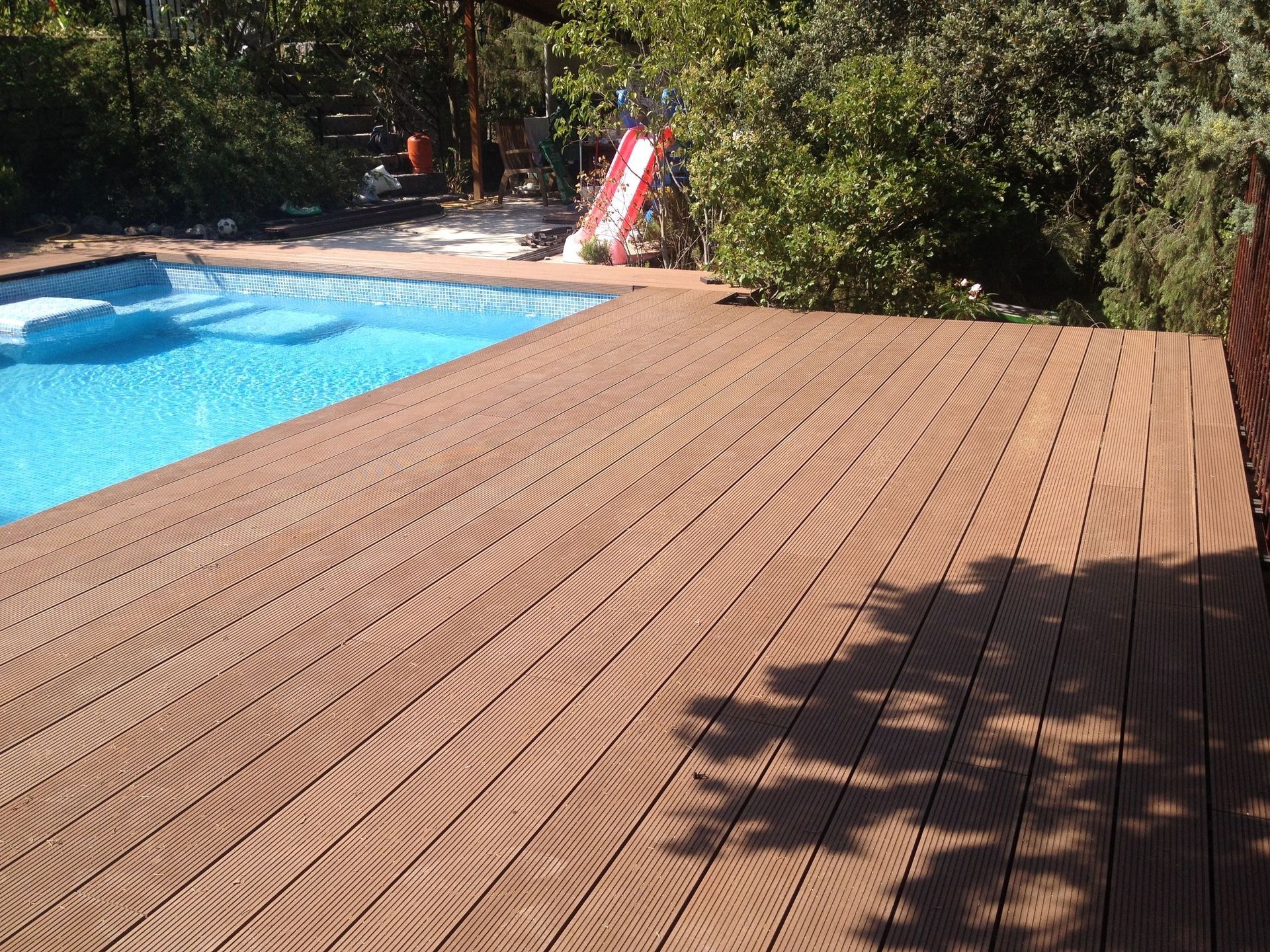 Una terraza de madera con una piscina al fondo.