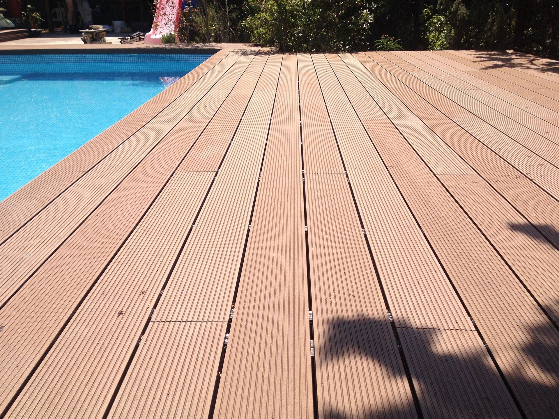 Una terraza de madera con una piscina al fondo.