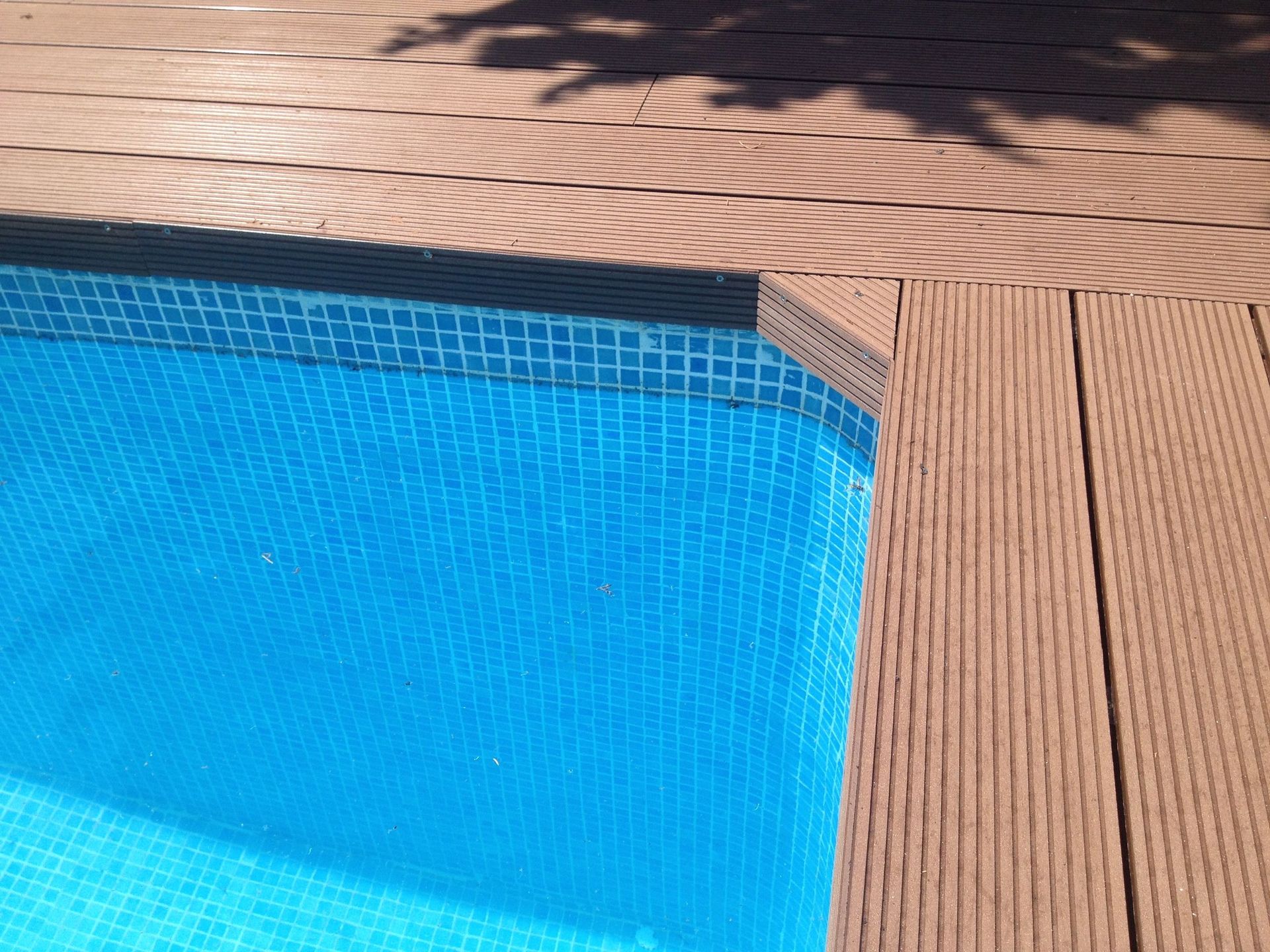 Una piscina con azulejos azules y una terraza de madera