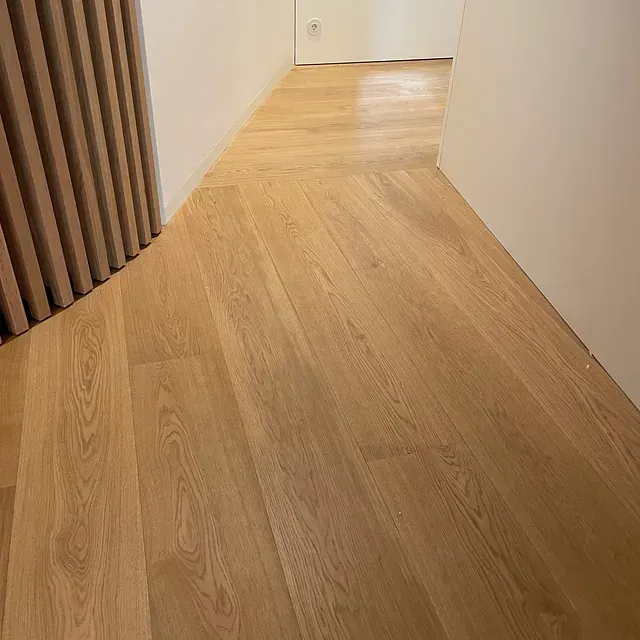 Un pasillo con suelo de madera y pared blanca.