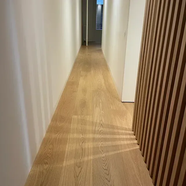 Un largo pasillo con suelo de madera y paredes blancas.