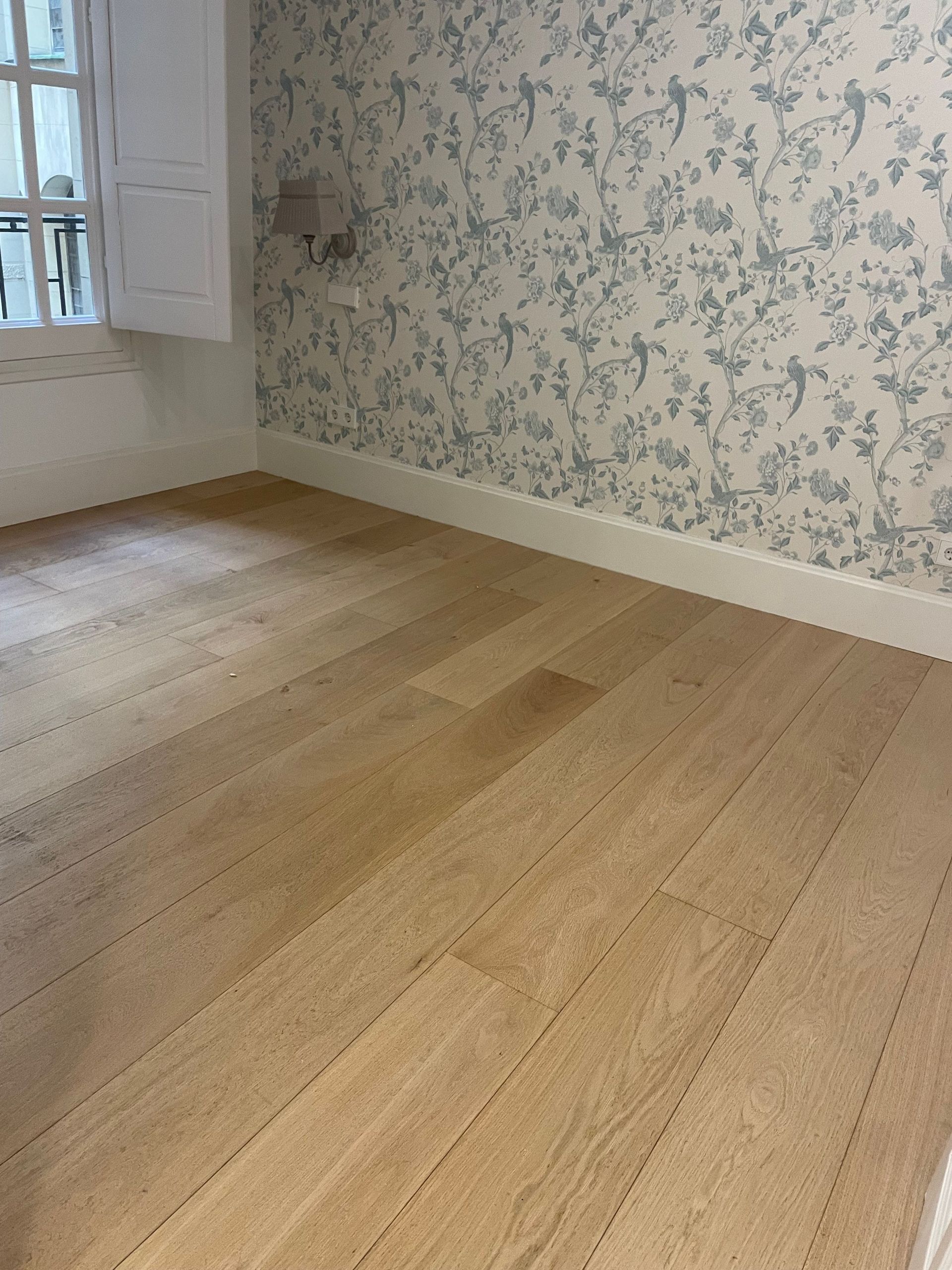 Una habitación vacía con suelo de madera y papel pintado floral.