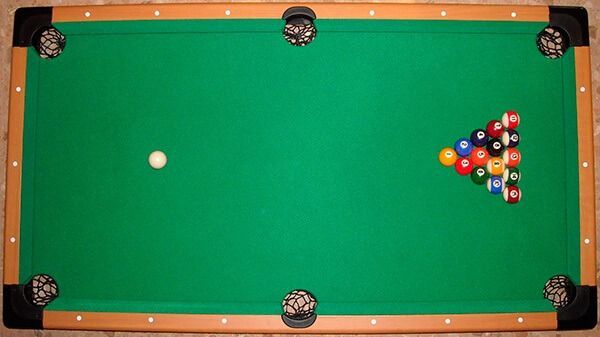 Vista aérea de una mesa de billar verde con la bola blanca y un juego de bolas listo para jugar.