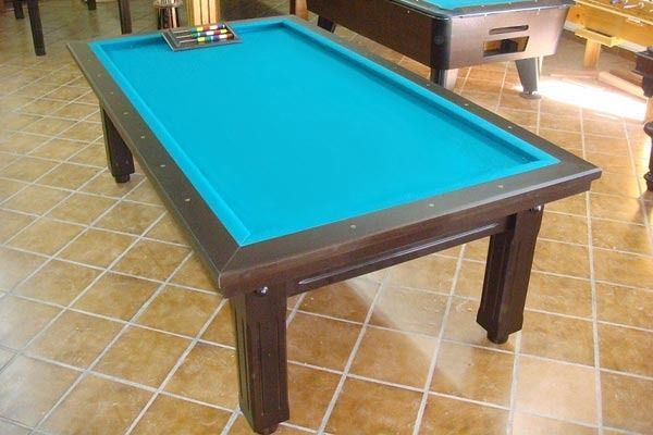 Una mesa de billar rectangular con tablero de fieltro azul y marco de madera marrón. Se ven bolas de billar en la parte superior.