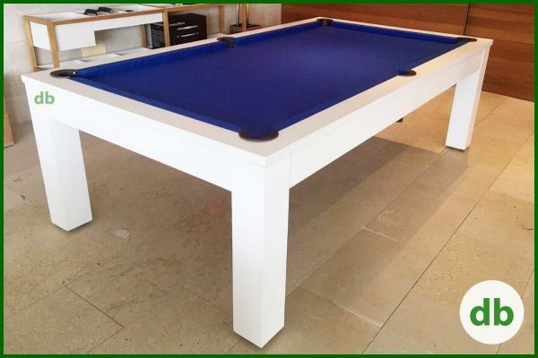 Mesa de billar blanca con superficie de fieltro azul y patas modernas a juego, en una habitación con suelo de baldosas.