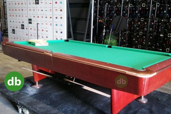 Mesa de billar con fieltro verde y marco de madera marrón en zona de almacenamiento.