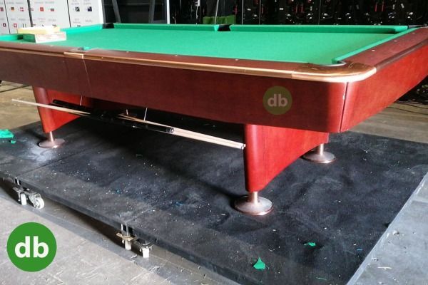 Una mesa de billar roja y verde con detalles de latón, en el interior sobre un tapete negro, con el logotipo