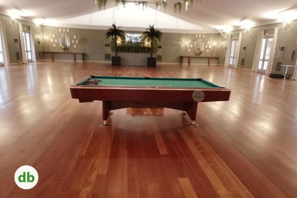 Una habitación espaciosa con suelos de madera pulida, mesa de billar y elementos decorativos. El ambiente es elegante y acogedor.