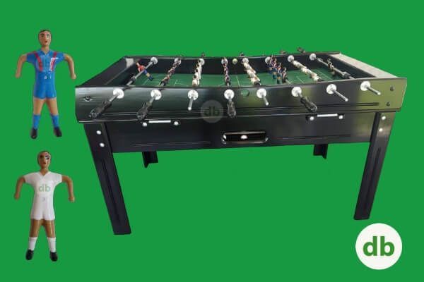 Mesa de futbolín en color negro con dos figuras de jugadores, una azul y otra blanca, sobre fondo verde.