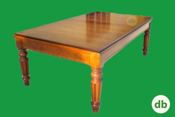 Mesa de comedor rectangular de madera con patas ornamentadas, sobre un fondo verde.