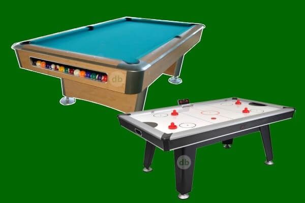 Una mesa de billar y una de air hockey, una junto a la otra, sobre un fondo verde. La mesa de billar es de madera con una superficie azul. La mesa de air hockey es blanca y negra.