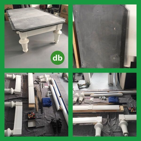 Una mesa de billar desmontada con patas blancas, tablero de fieltro gris y piezas dispersas. Las piezas yacen sobre una superficie gris en un taller.