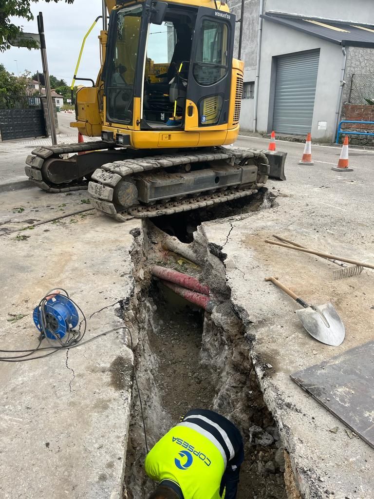 Un hombre está cavando un hoyo en el suelo al lado de una excavadora amarilla.