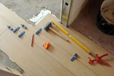 Herramientas y materiales para el suelo de madera dispuestos para la instalación, incluyendo un nivel y un martillo.