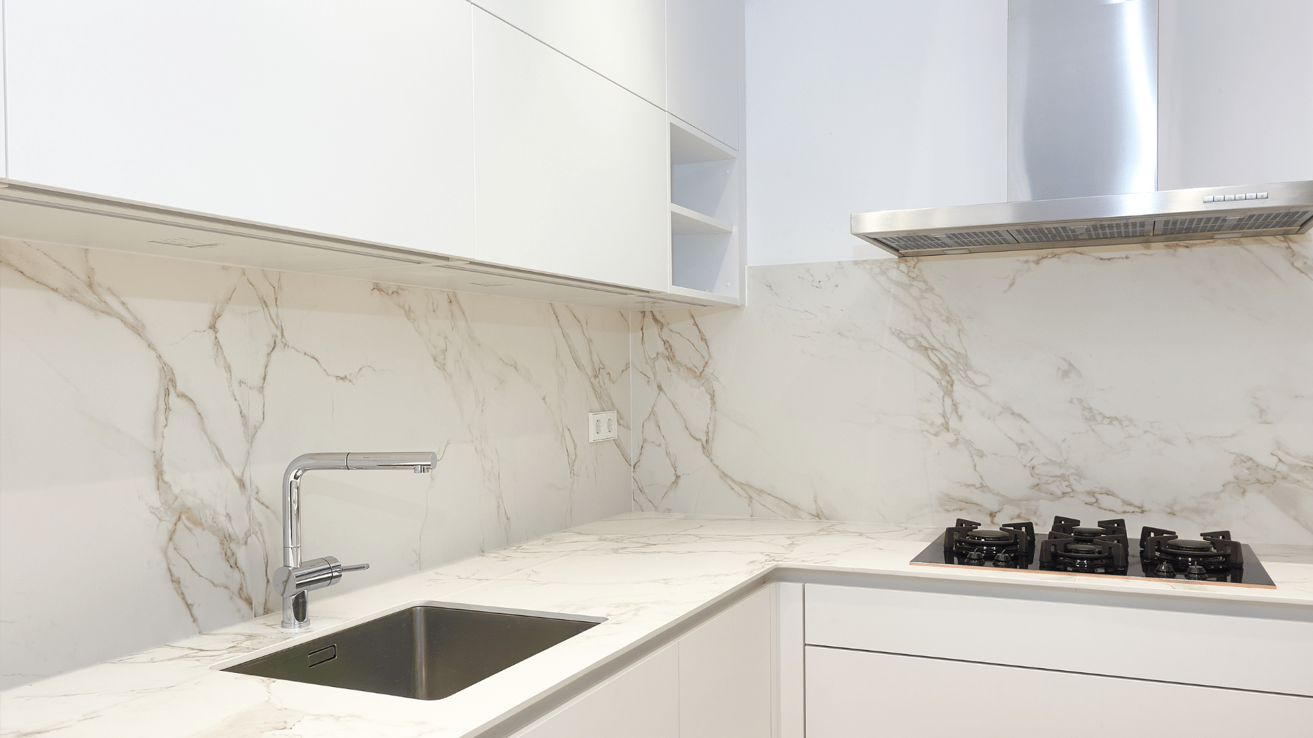 Cocina blanca con salpicadero de mármol, fregadero de acero inoxidable y placa de cocina.