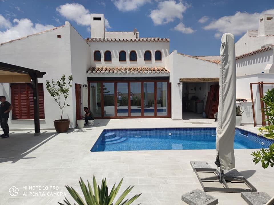 Villa blanca con piscina, puertas plegables con marco de madera, cielo azul.