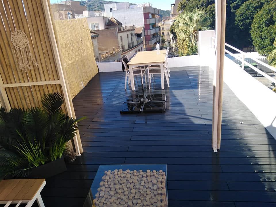 Terraza en la azotea con mesa, sillas, plantas y vistas a la ciudad. Terraza de madera, barandilla blanca y biombo de bambú.