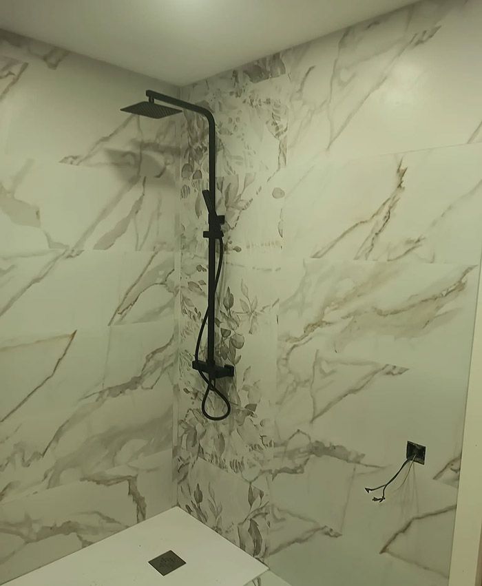 Grifo de ducha negro sobre pared alicatada con aspecto de mármol blanco en una cabina de ducha.