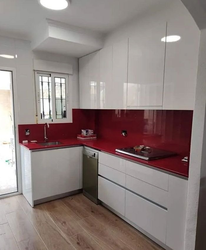Cocina moderna blanca con salpicadero rojo, electrodomésticos de acero inoxidable y suelo de madera.