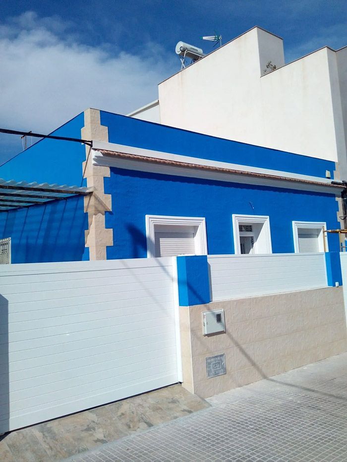 Edificio azul y blanco con una valla a juego bajo un cielo azul.