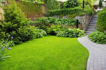Jardin luxuriant avec pelouse verte, allée en pierre, murs couverts de lierre et marches menant à flanc de colline