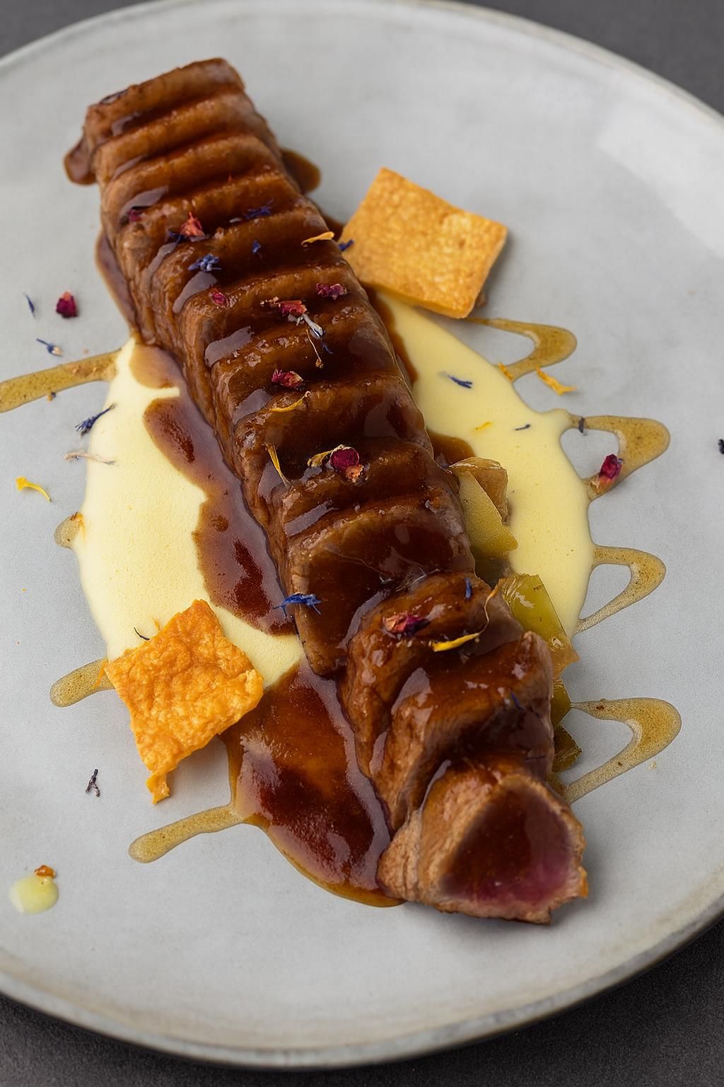 Sándwich abierto sobre plato marmolado, cubierto con flores de colores y un chorrito de salsa.