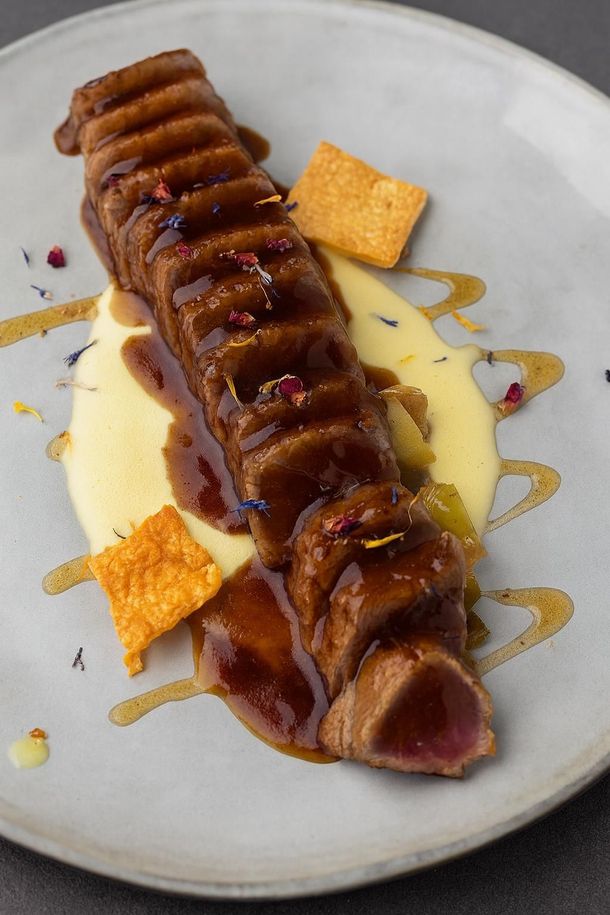 Sándwich abierto sobre plato marmolado, cubierto con flores de colores y un chorrito de salsa.