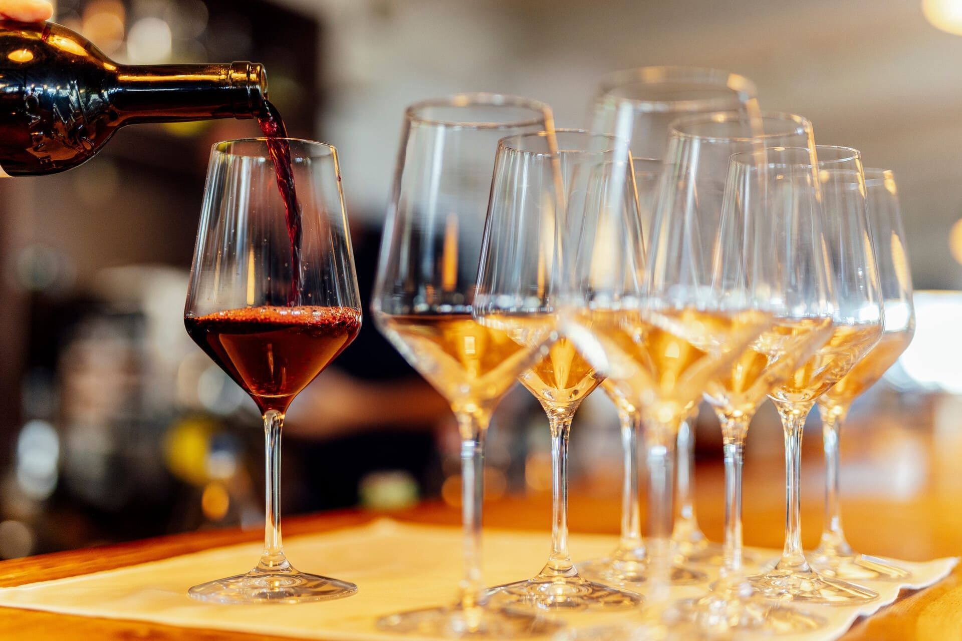 Se está sirviendo vino tinto en una copa entre varias copas de vino vacías sobre la barra de un bar.