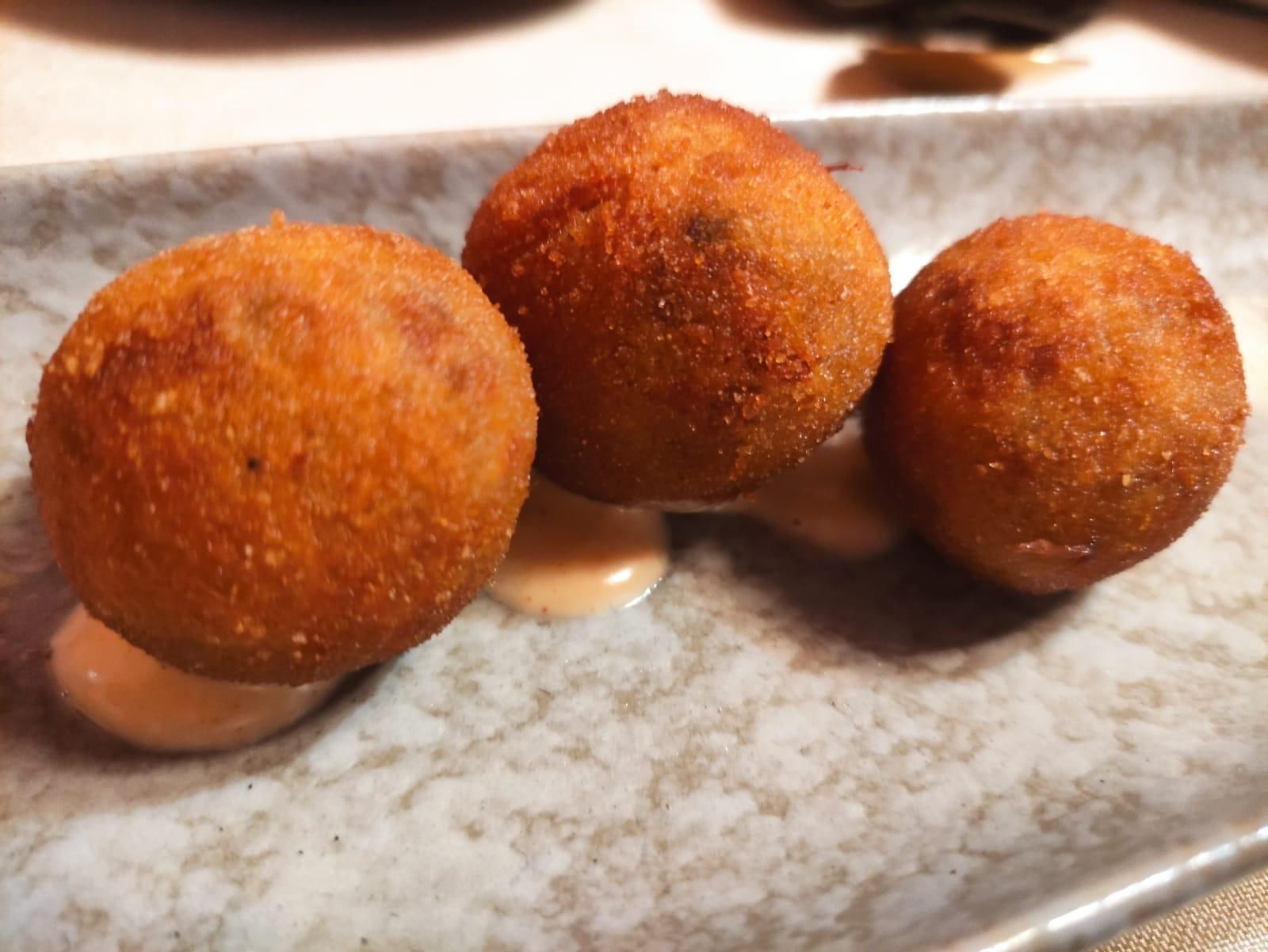 Tres croquetas doradas fritas en un plato, rociadas con una salsa de color claro.