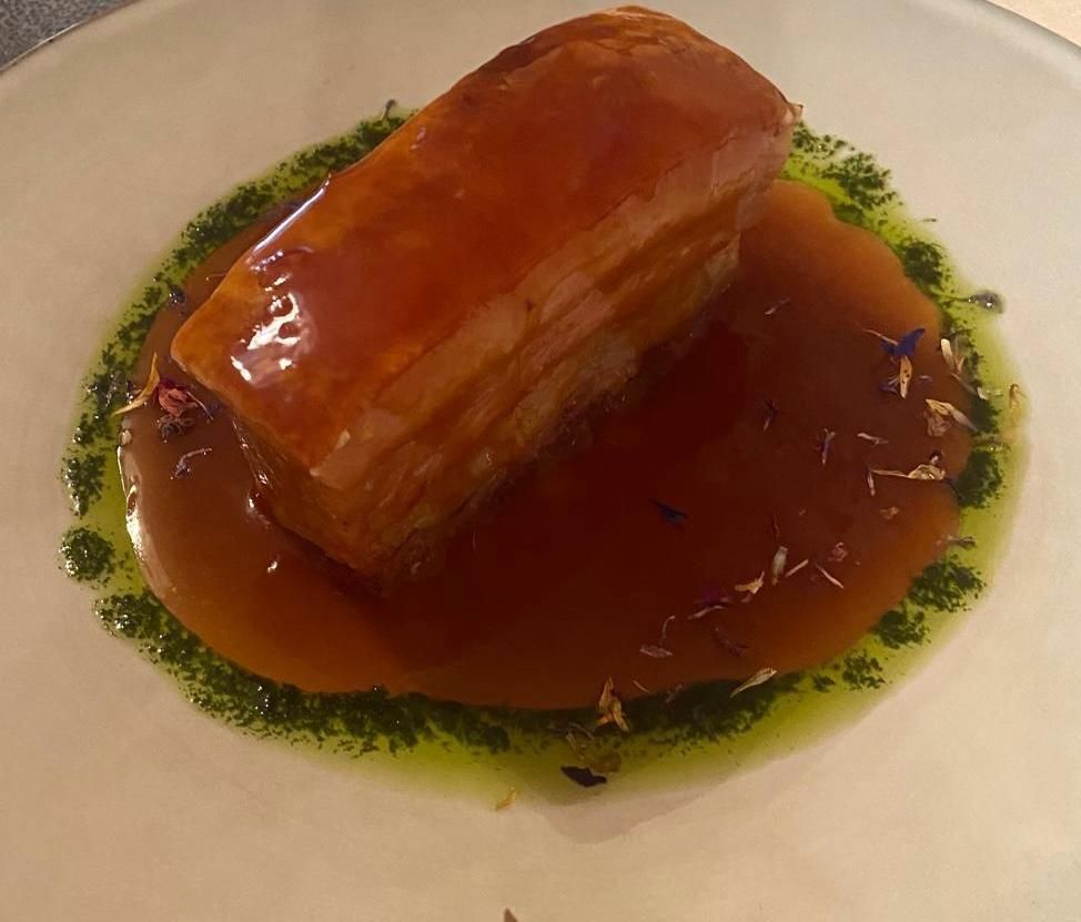 Panceta de cerdo estofada con salsa y guarnición verde en un plato blanco.