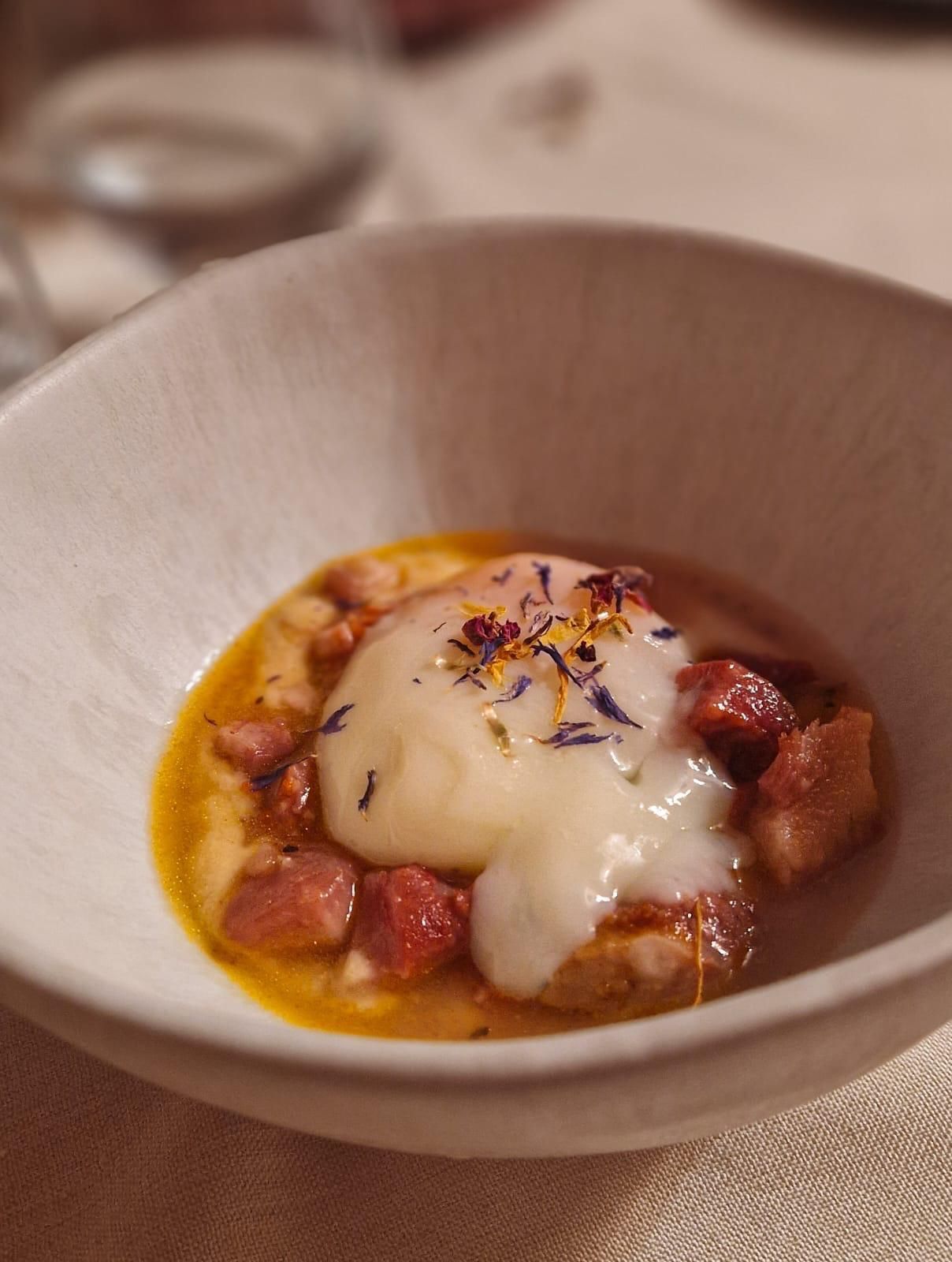 Cuenco blanco con huevo escalfado, carne cortada en cubitos y caldo, adornado con flores.