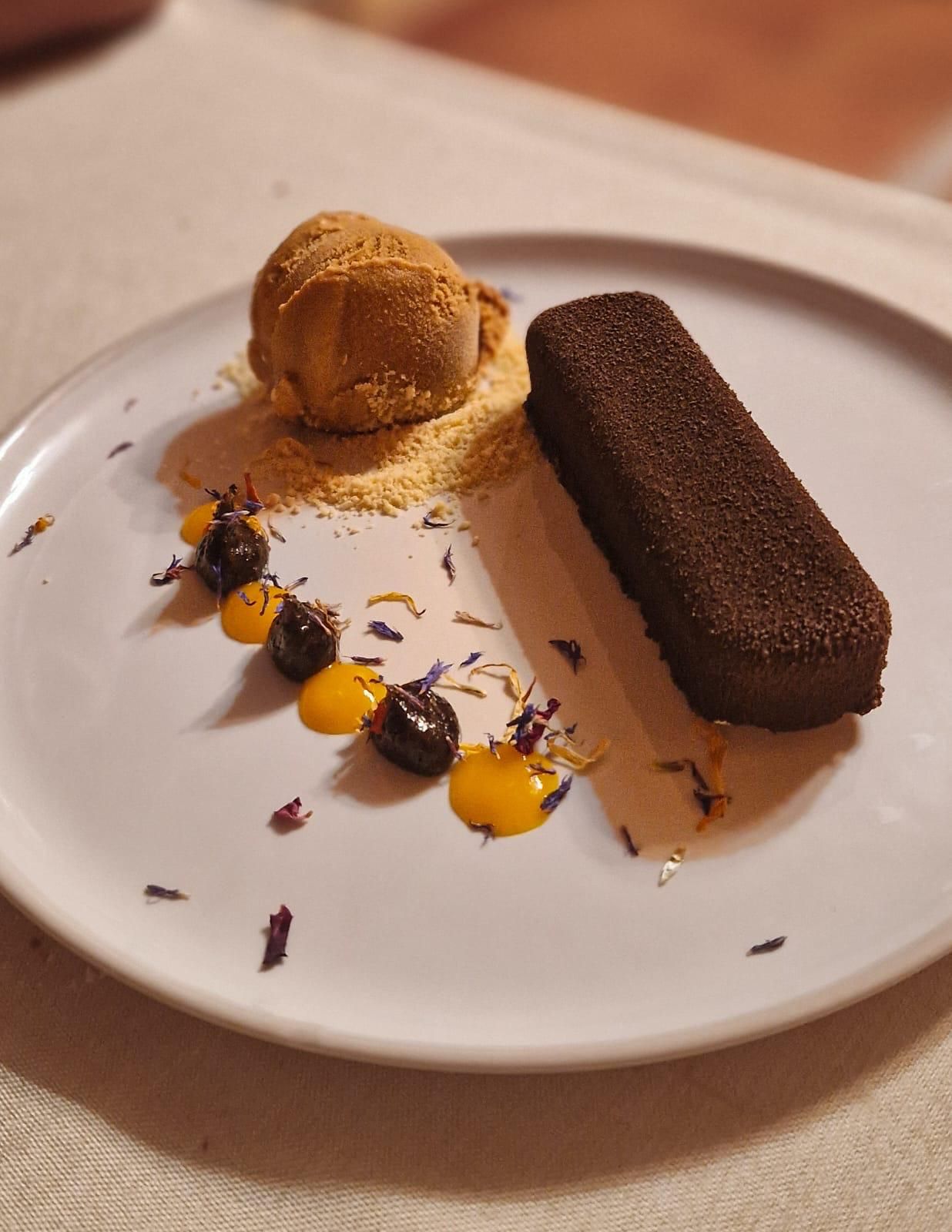 Plato de postre: tarta de chocolate, bola de helado, puntos de salsa, flores comestibles y migas.