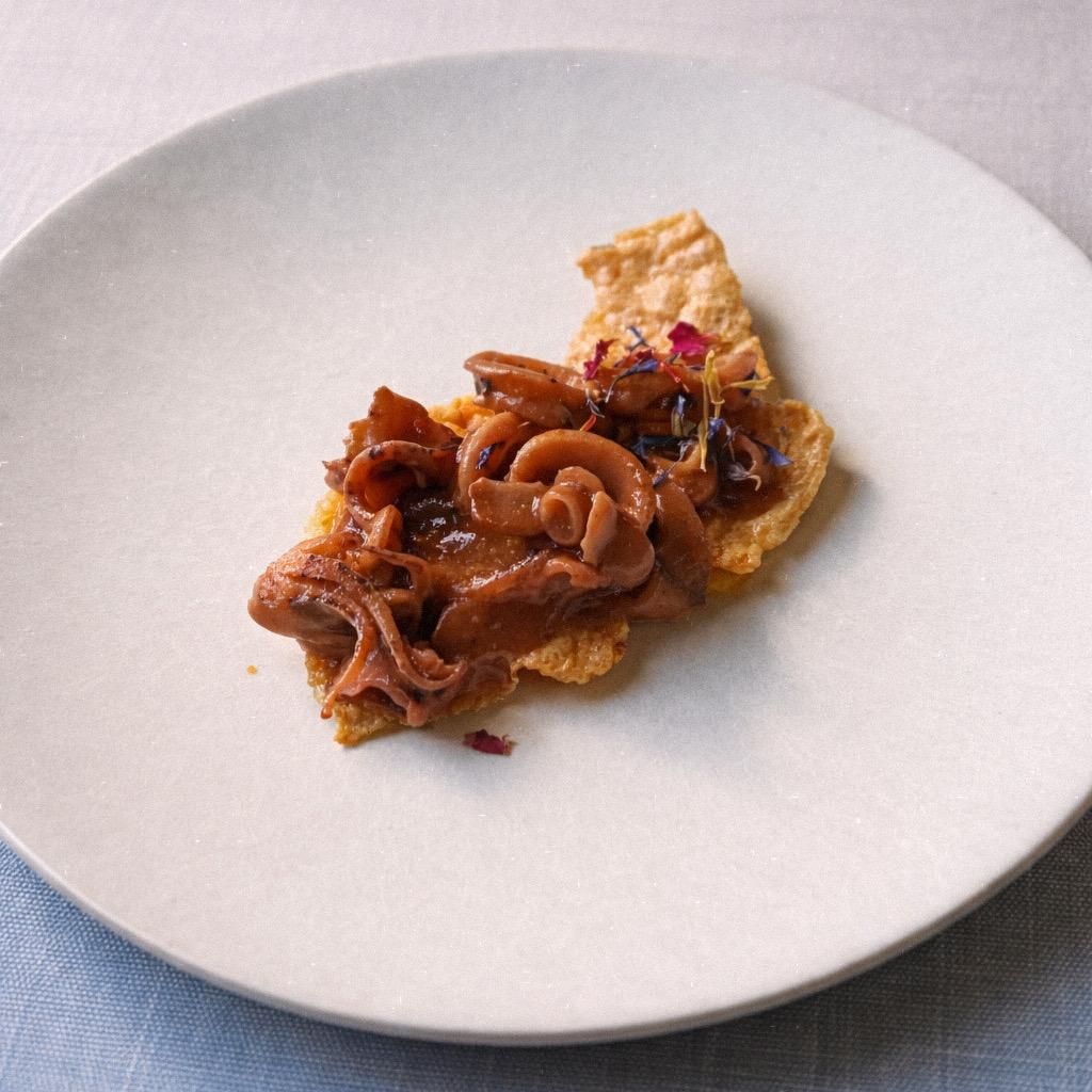 Plato de postre: tarta de chocolate, bola de helado, puntos de salsa, flores comestibles y migas.