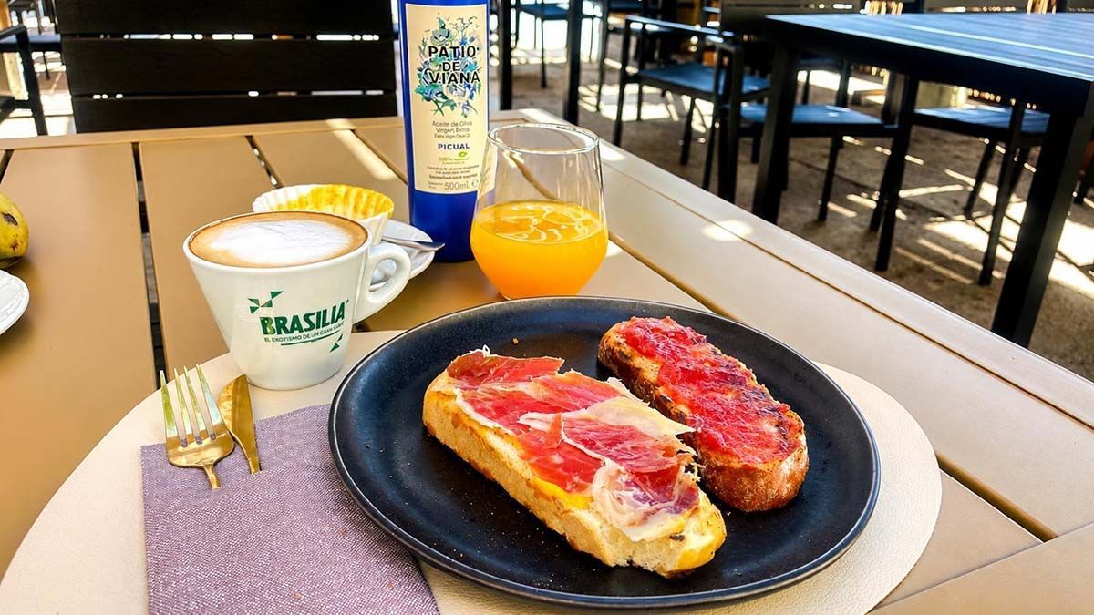 Bandeja de desayuno con bollería, yogur y zumo de naranja sobre una mesa en una cafetería.