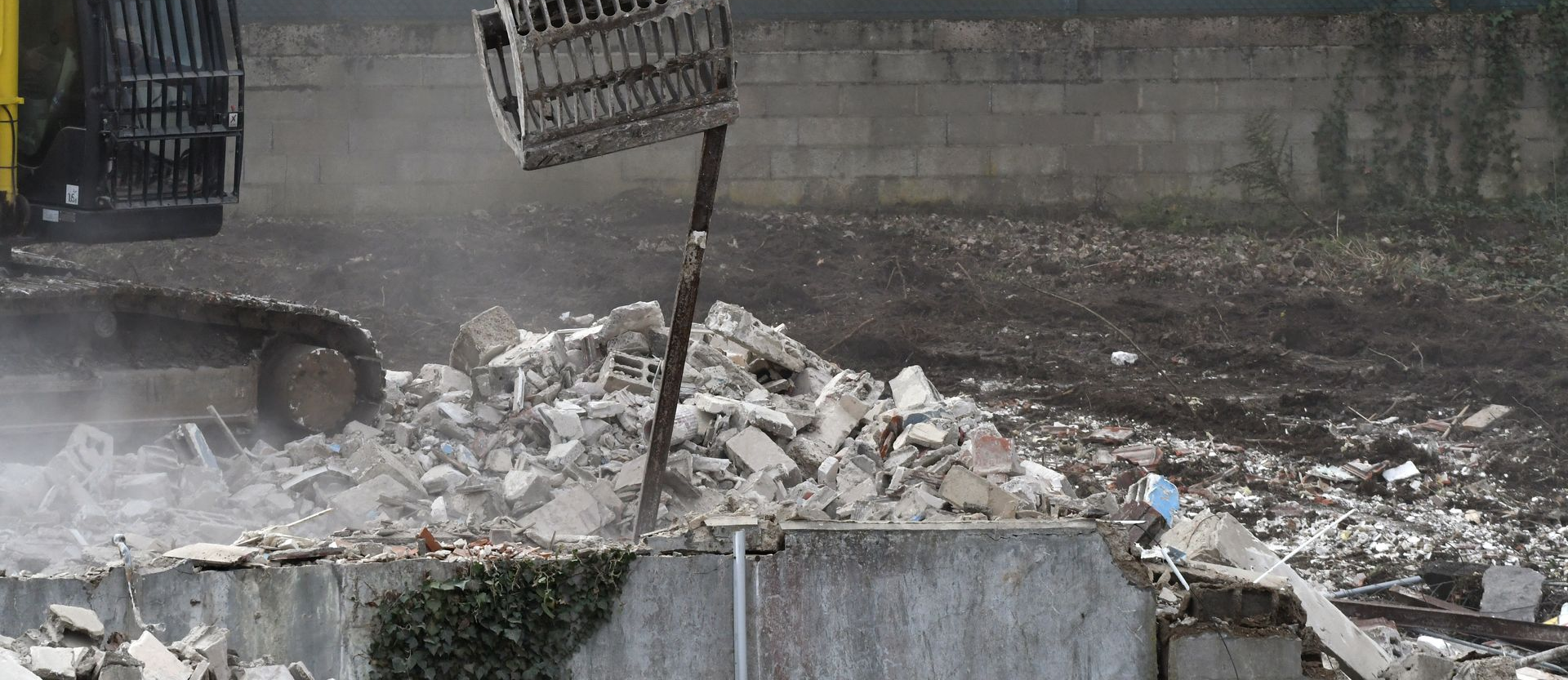 Une excavatrice équipée d'un concasseur hydraulique travaille sur un tas de gravats de béton sur un chantier de démolition.