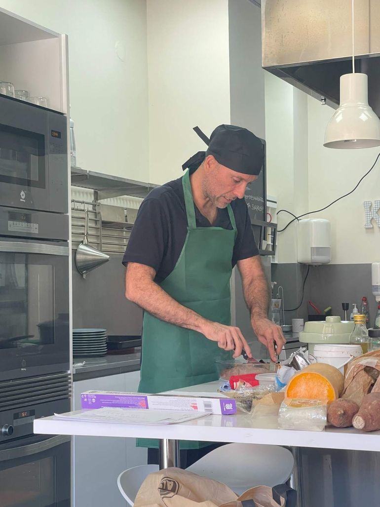 Una persona con un delantal verde cortando alimentos en una encimera de cocina, con pan e ingredientes cerca