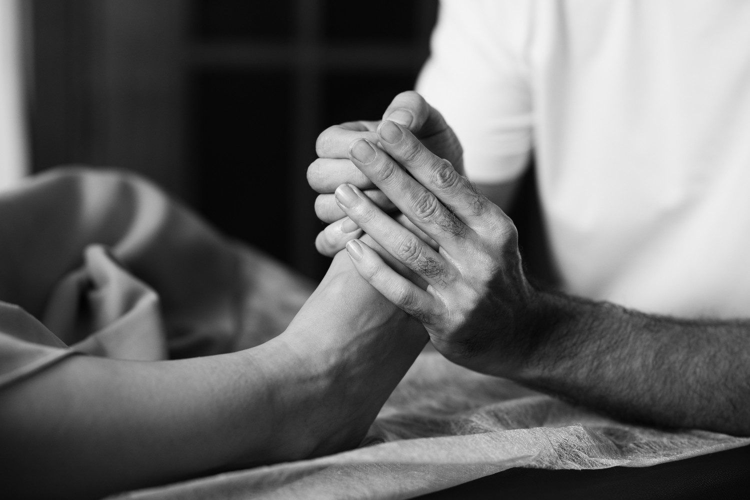Dos manos entrelazadas en señal de apoyo sobre una cama, una descansando sobre la otra, en blanco y negro.