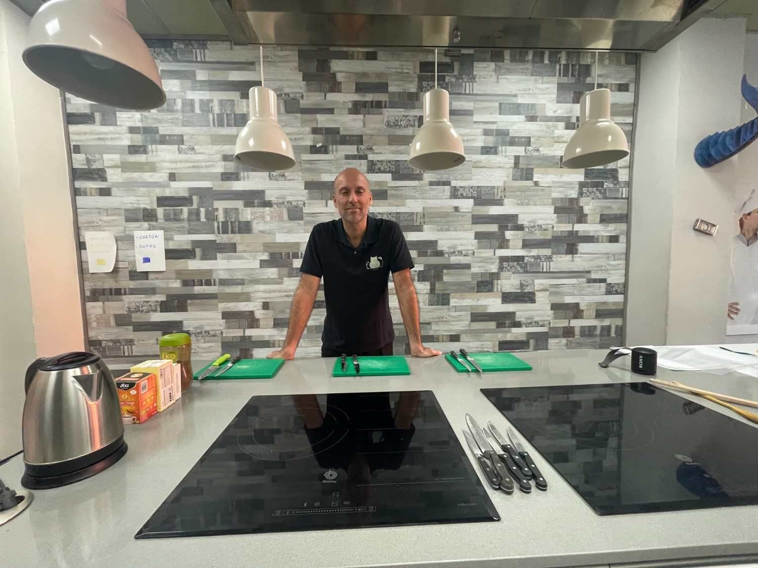 Una persona de pie detrás de una isla de cocina con placas de cocción negras, en una cocina moderna