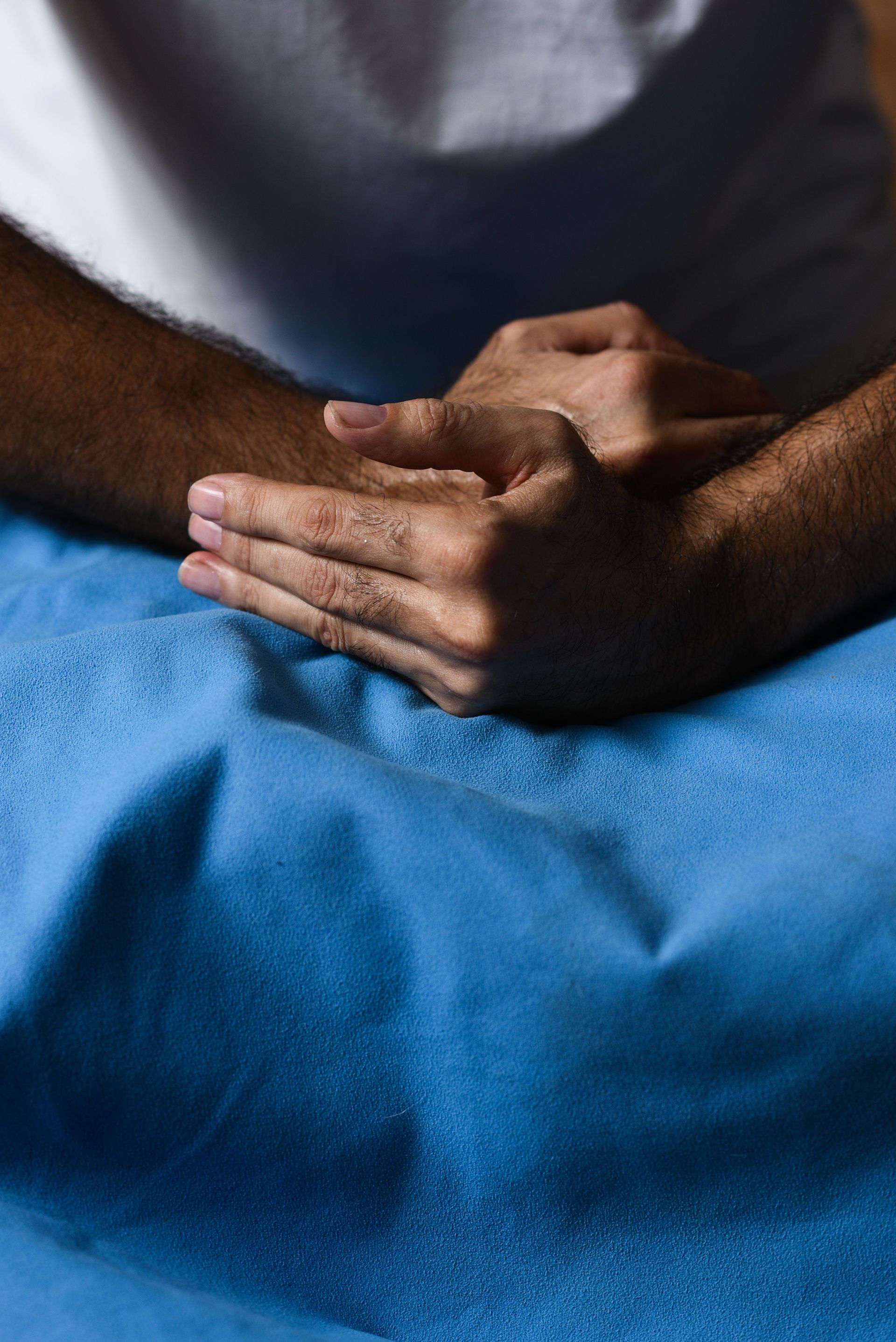 Un hombre yace sobre una manta azul con las manos juntas.